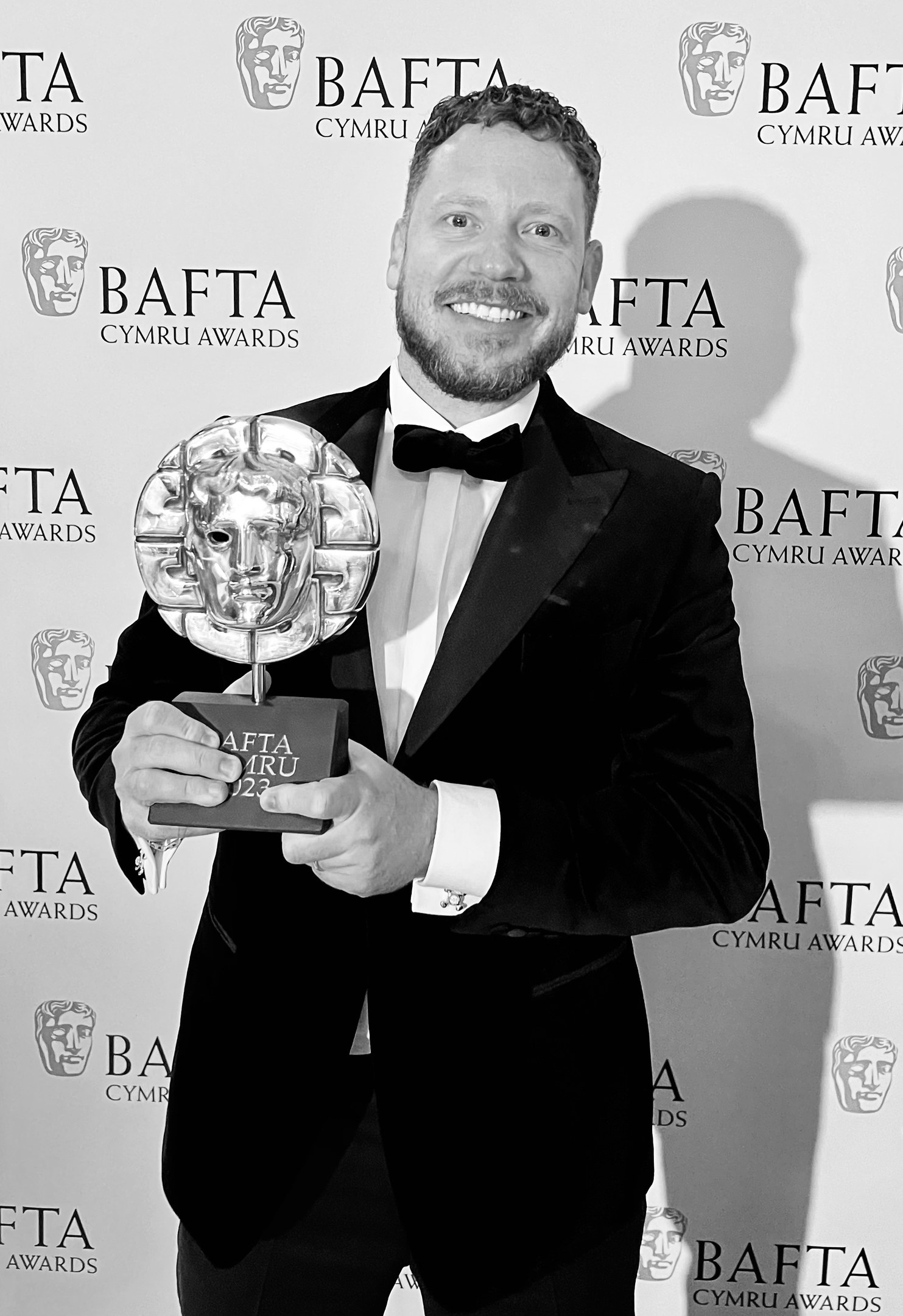 Ein Mann im Smoking, der eine BAFTA-Trophäe hält und lächelt, mit einem Hintergrundbanner, auf dem "BAFTA Awards 2018" steht.