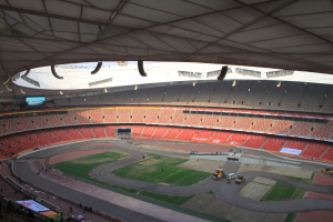 Großes Stadion voller Menschen, Fahrzeuge auf der Straße, grüner Boden, Texttafeln, Geländer, ein Bildschirm und Deckenbeleuchtung.
