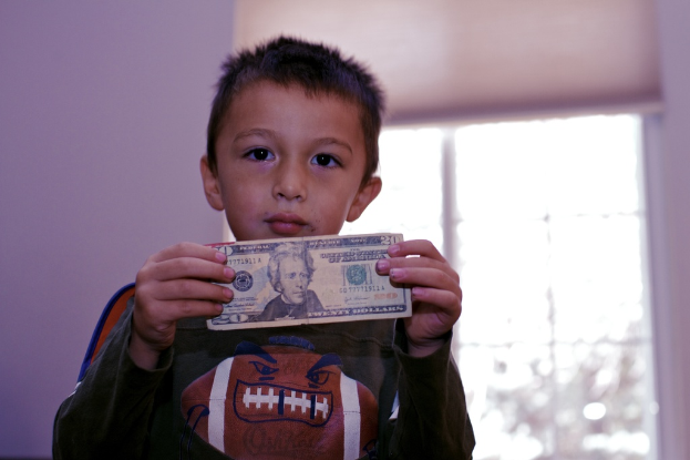Ein Junge hält Geld in den Händen, im Hintergrund ist ein Fenster und eine Wand zu sehen.